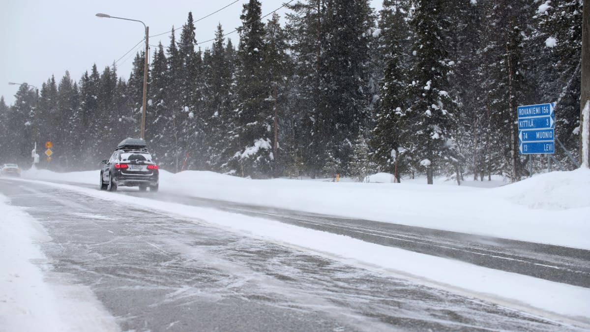 Auto ajaa talvisella tiellä, lumi pöllyää.