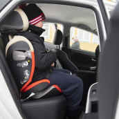 Kouluikäinen lapsi istuu turvaistuimessa pysäköidyn henkilöauton kyydissä.
