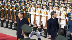 Kiinan Xi on kääntyneenä kuvassa vasemmalla, Ranskan Macron oikealle kiinalaisten naissotilaiden rivistöjen edessä. Kummallakin on vakava ilme.