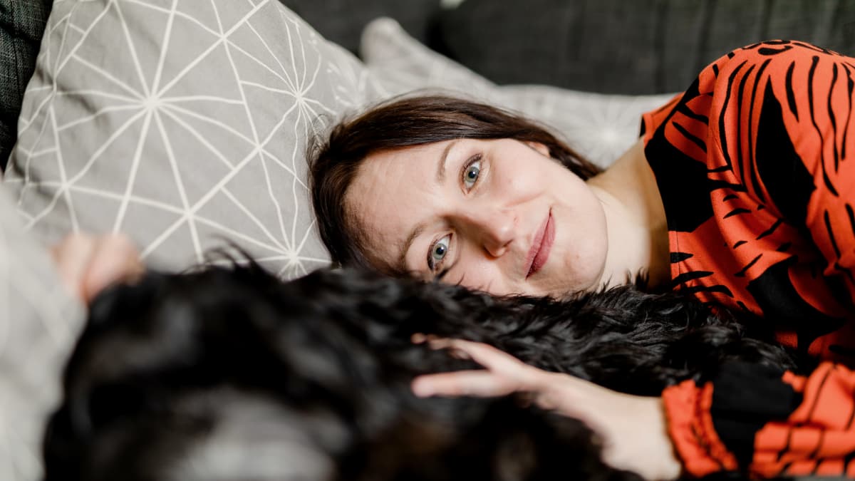 Tiina Raevaara makoilee sohvalla mustan villakoiran kanssa.