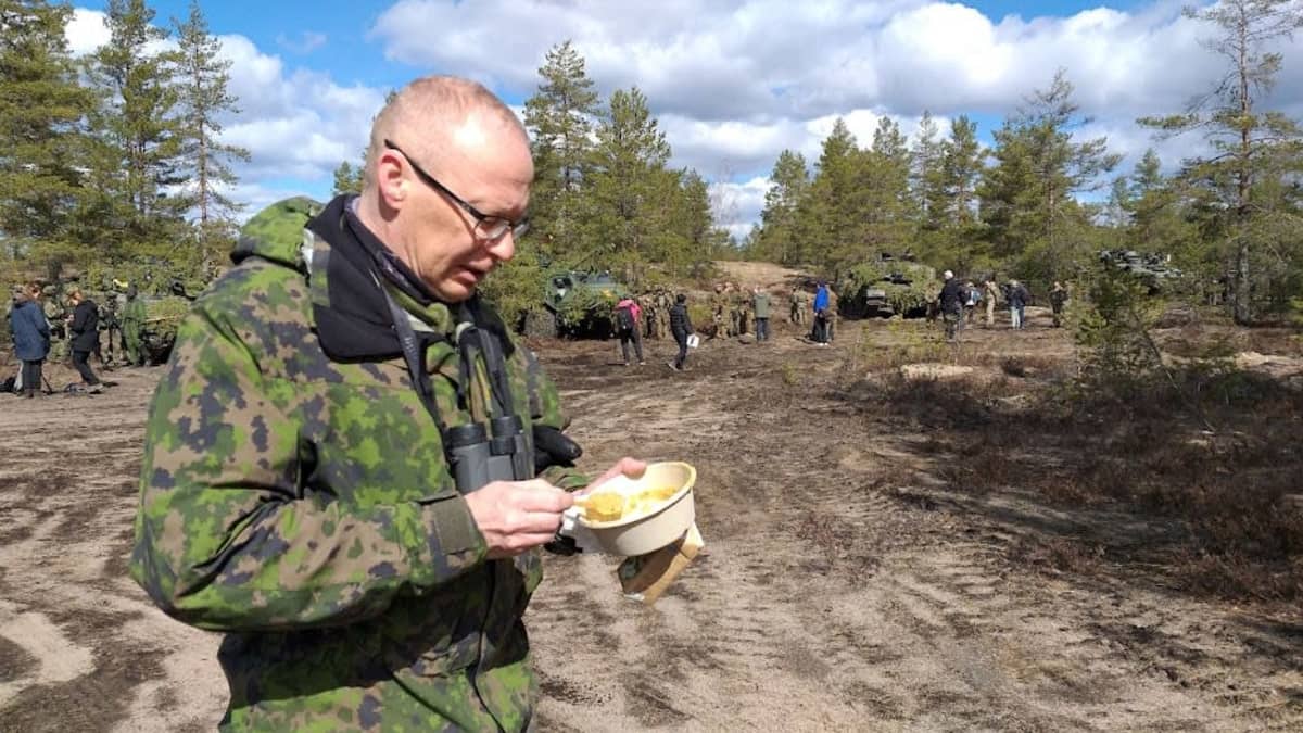 Hiekkaisen kangasmetsikön aukealla sotilaspukuinen mies syö keittoa kertakäyttölautaselta. 
