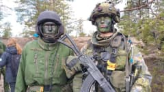 Kaksi vihreän kasvovärin avulla naamioitunutta sotilasta seisoo rinnkkain. Toisella rinnalla rynnäkkökivääri. 