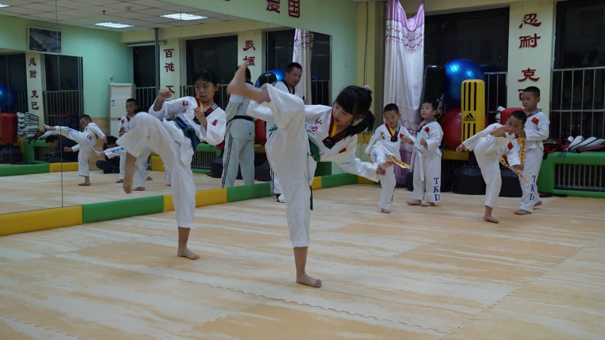 Wei Yong ohjaa lasten taekwondo-tuntia. lapset harjoittelevat potkuja valkoisissa puvuissa.