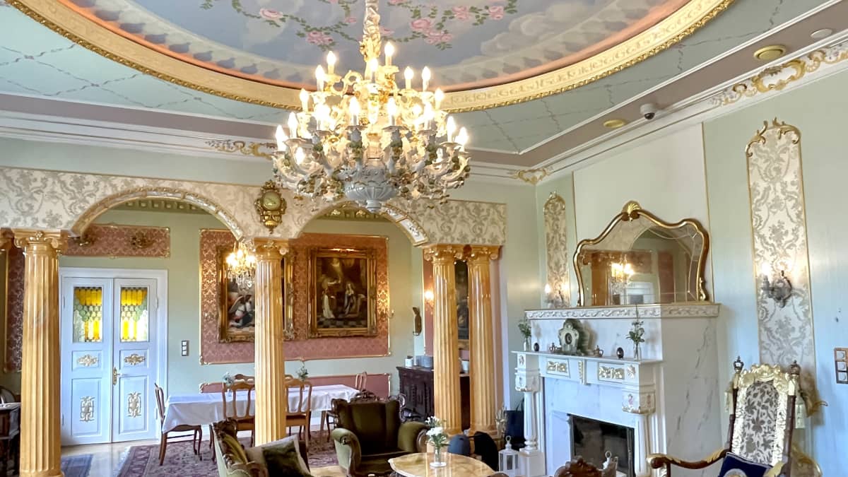 Villa Royalin kuninkaallisella tyylillä sisustettu sisätila. Huoneessa hienot tuolit, pöydät, takka ja kattokruunu ja -maalaukset.