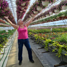 Puutarhayrittäjä Pia Kohvakka Katajankankaan puutarhalta seisoo kädet kohti taivasta kukkien keskellä.