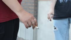 Närbild på två personers händer, de håller i cigaretter.