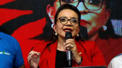 En kvinna i röd jacka håller tal.