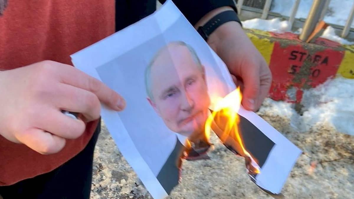Henkilö pitää kädessään palavaa Vladimir Putinin valokuvaa.