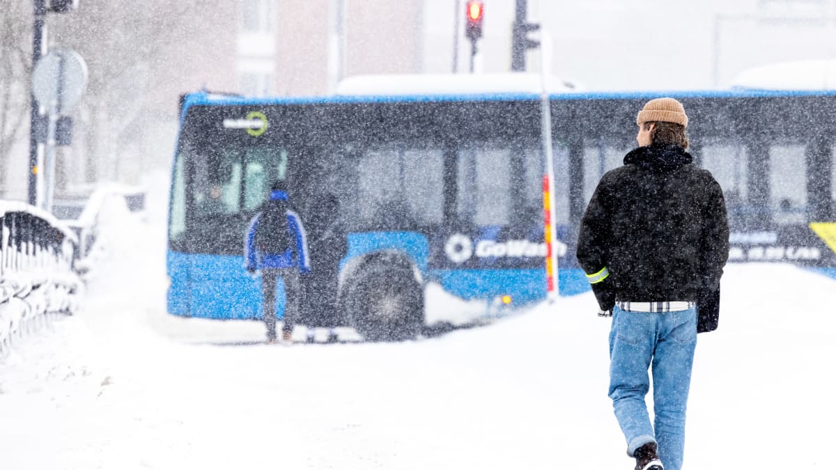 Henkilö kävelee sankassa lumisateessa taustalla näkyy bussi.