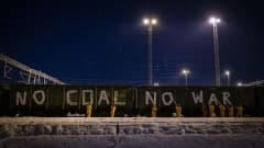 keltapukuiset ihmiset maalaavat junavaunujen seiniin valkoista tekstiä: no coal no war.