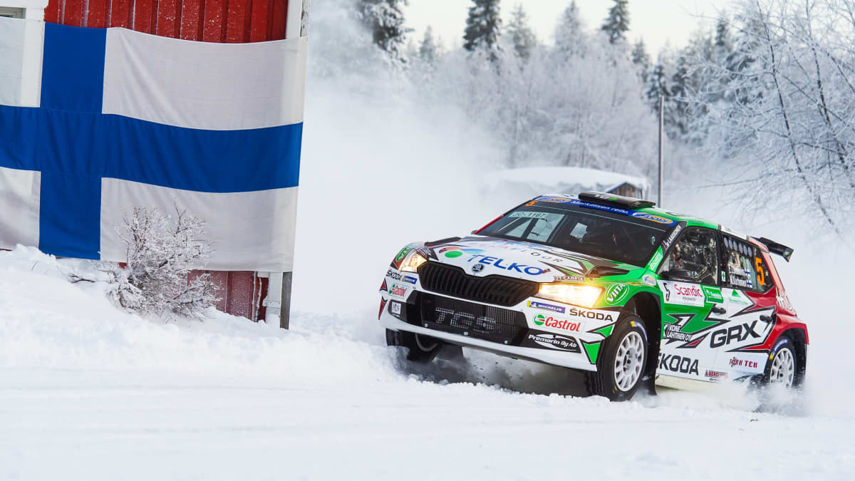 En rallybil kommer fort i en kurva på snötäckt väg.