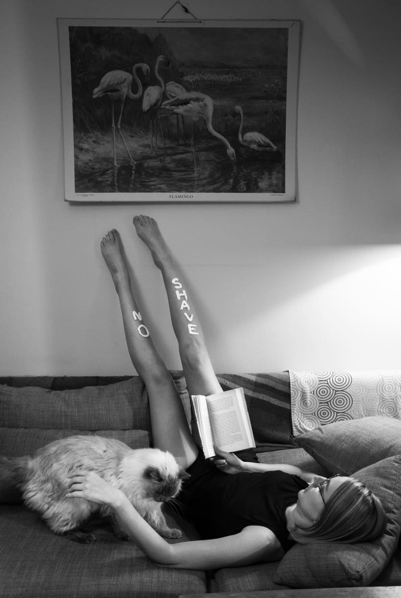 Kati Ojala makaa sohvalla kissan kanssa ja lukee kirjaa, jalat pystyssä vasten seinää.