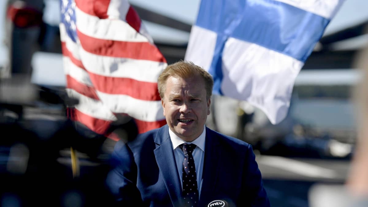 Antti Kaikkonen puhuu tiedotustilaisuudessa. Taustalla Suomen ja Yhdysvaltain liput.