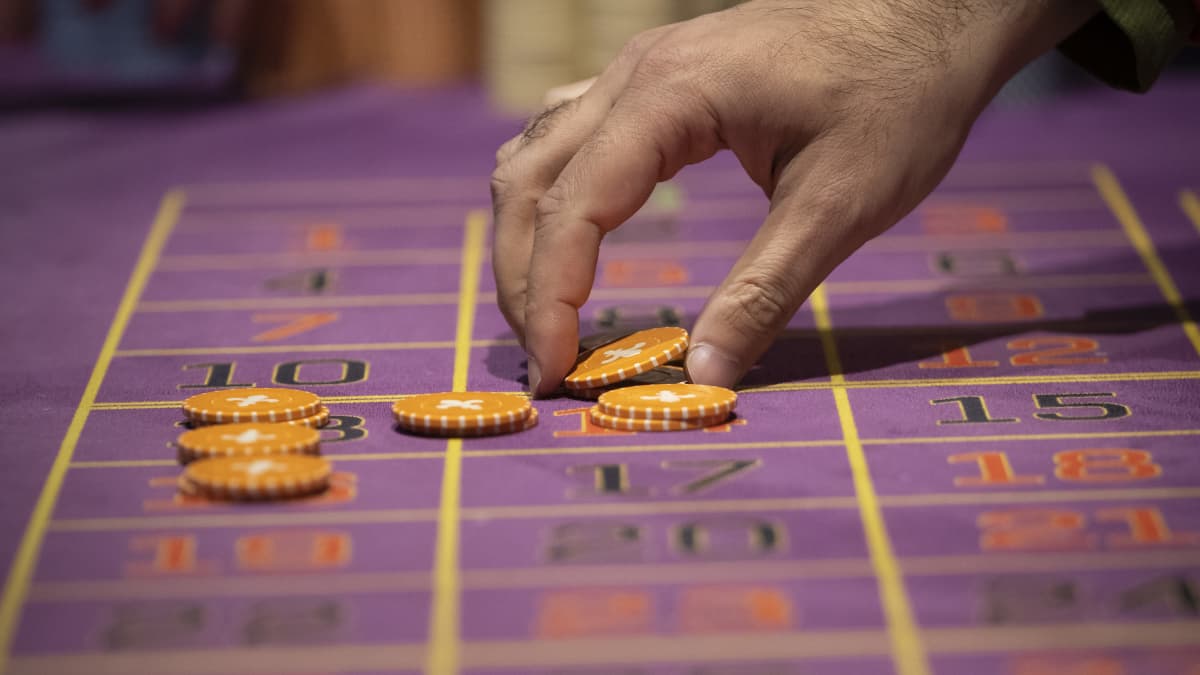Lähikuva kädestä asettamassa panoksia pelipöytään kasinolla.