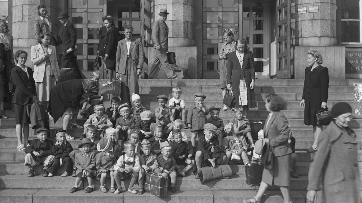 Ruotsista palaavia sotalapsia istuu Helsingin rautatieaseman portailla.