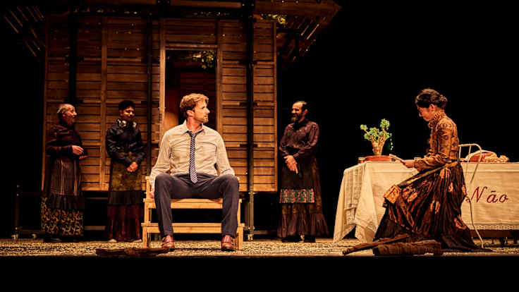 Teatteriesitys: näyttämöllä mies ja nainen istuvat vastakkain. Naisella käsissään paperi.