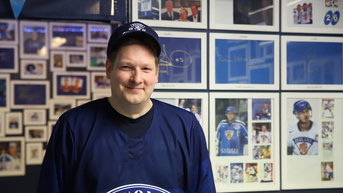 Juha Pitkäniemi hymyilee kameralle Leijonat-seinän edessä.