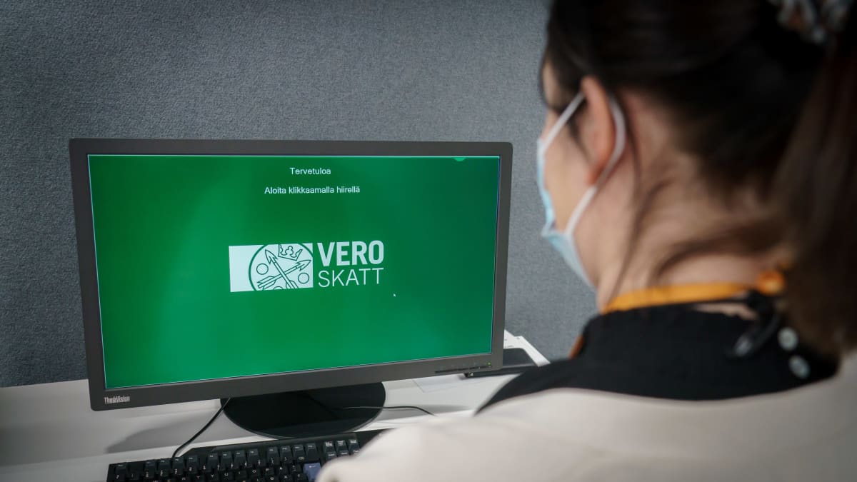 Naishenkilö verotoimistossa käyttämässä tietokonetta, jonka vihreällä näytöllä näkyy verohallinnon logo.