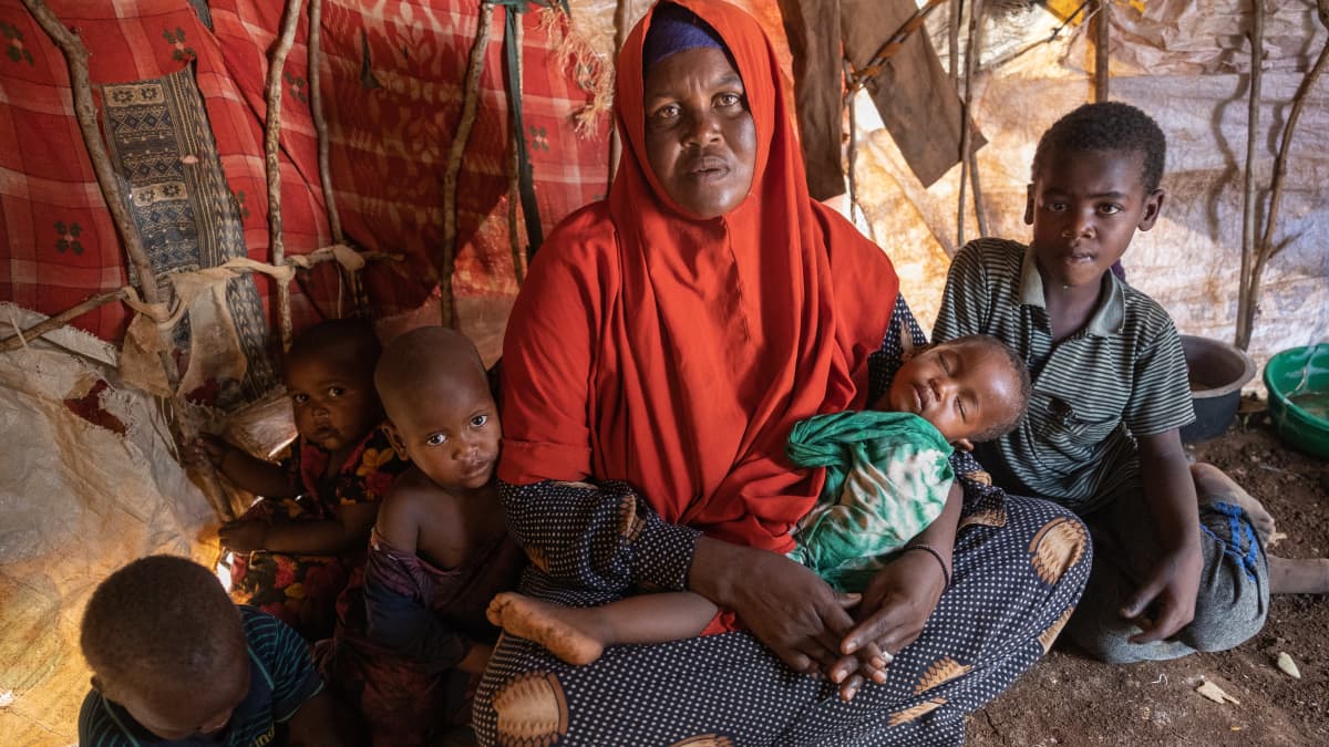 Somalialainen pakolaisäiti Adey Isak teltassa punaisessa hunnussa viiden lapsensa kanssa, surumielisen oloisena. 