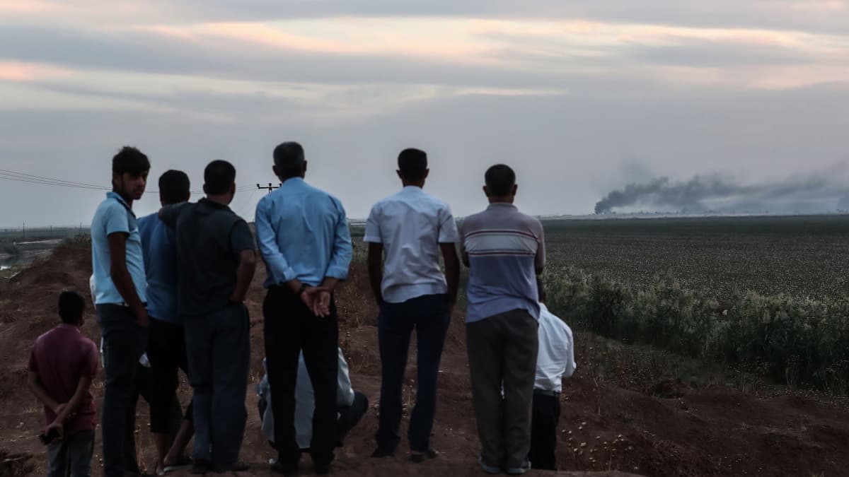  Miehet katsovat Turkin puolelta rajaa, kun Syyrian puolella Tel Abyadin kaupungissa savuaa iskujen jäljiltä.
