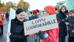 Kaksi mielenosoittajaa hymyilee. Kyltissä lukee loppu luontokadulle