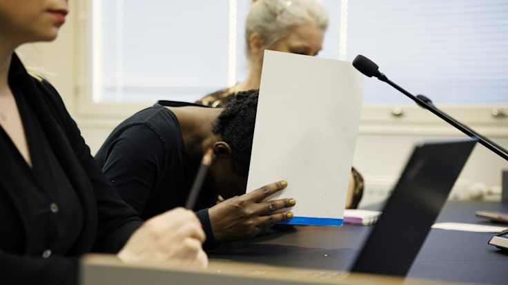 A suspect in court, trying to hide her face from photographers with a pad of paper.