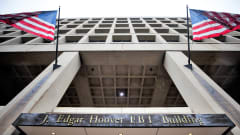 Kaksi Yhdysvaltain lippua liehuu FBI:n päämajan julkisivulla. Kyltissä lukee J. Edgar Hoover FBI Building. Kuva on otettu alaviistosta ylöspäin pitkin julkisivua.