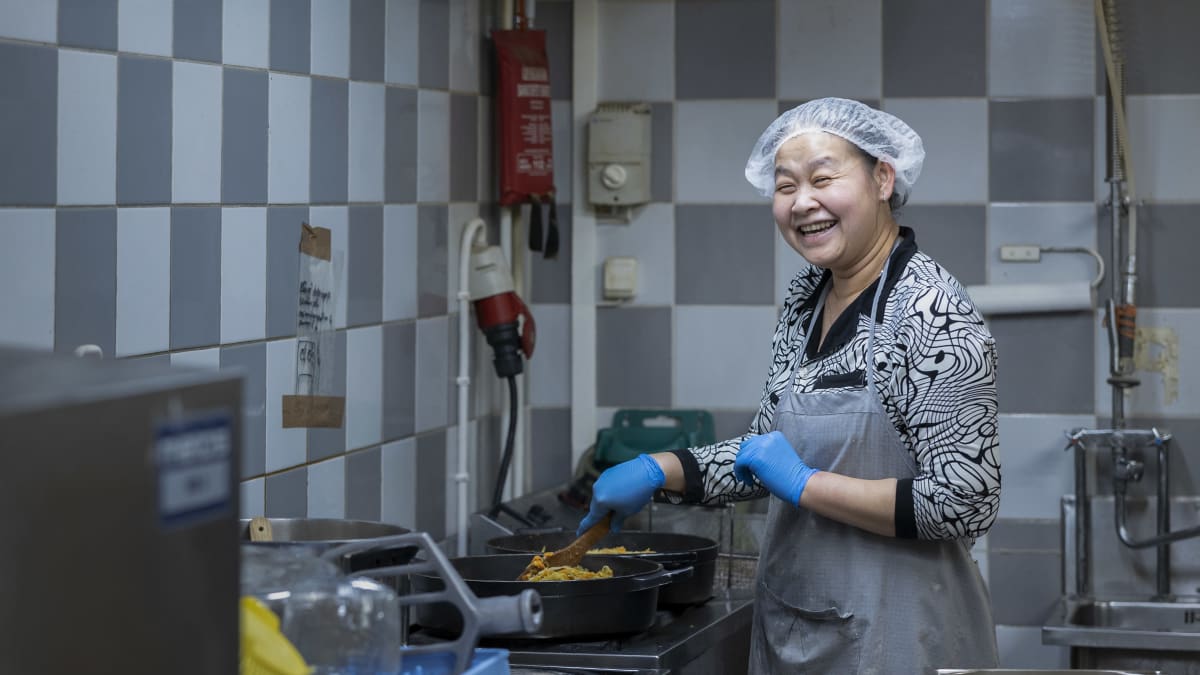 My Duyen Ho sekoittaa hymyillen paistinpannulla paistuvaa lihapiirakoiden täytettä Karjalaisen kotileipomossa. Hänellä on päässään suojamyssy ja kädessä kumihansikkaat. 