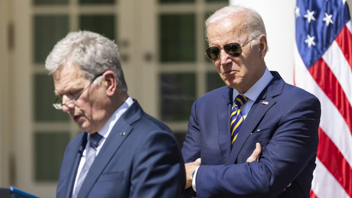 Yhdysvaltojen presidentti Joe Biden seisoo kädet ristissä presidentti Sauli Niinistön vieressä. Bidenilla on päällään puku ja päässään pilottilasit. Suomen tasavallan presidentti Sauli Niinistö pitää puhetta.
