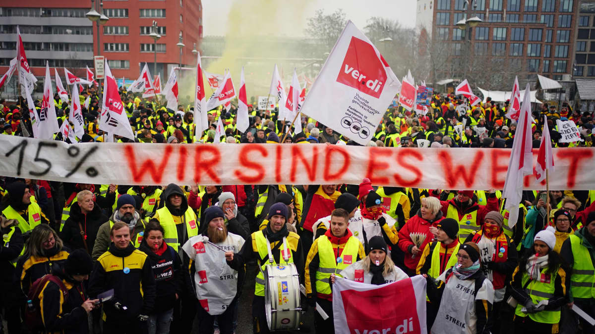 Keltaliivisiä mielenosoittajia ja kyltti, jossa lukee "15%, OLEMME SEN ARVOISIA" saksaksi.