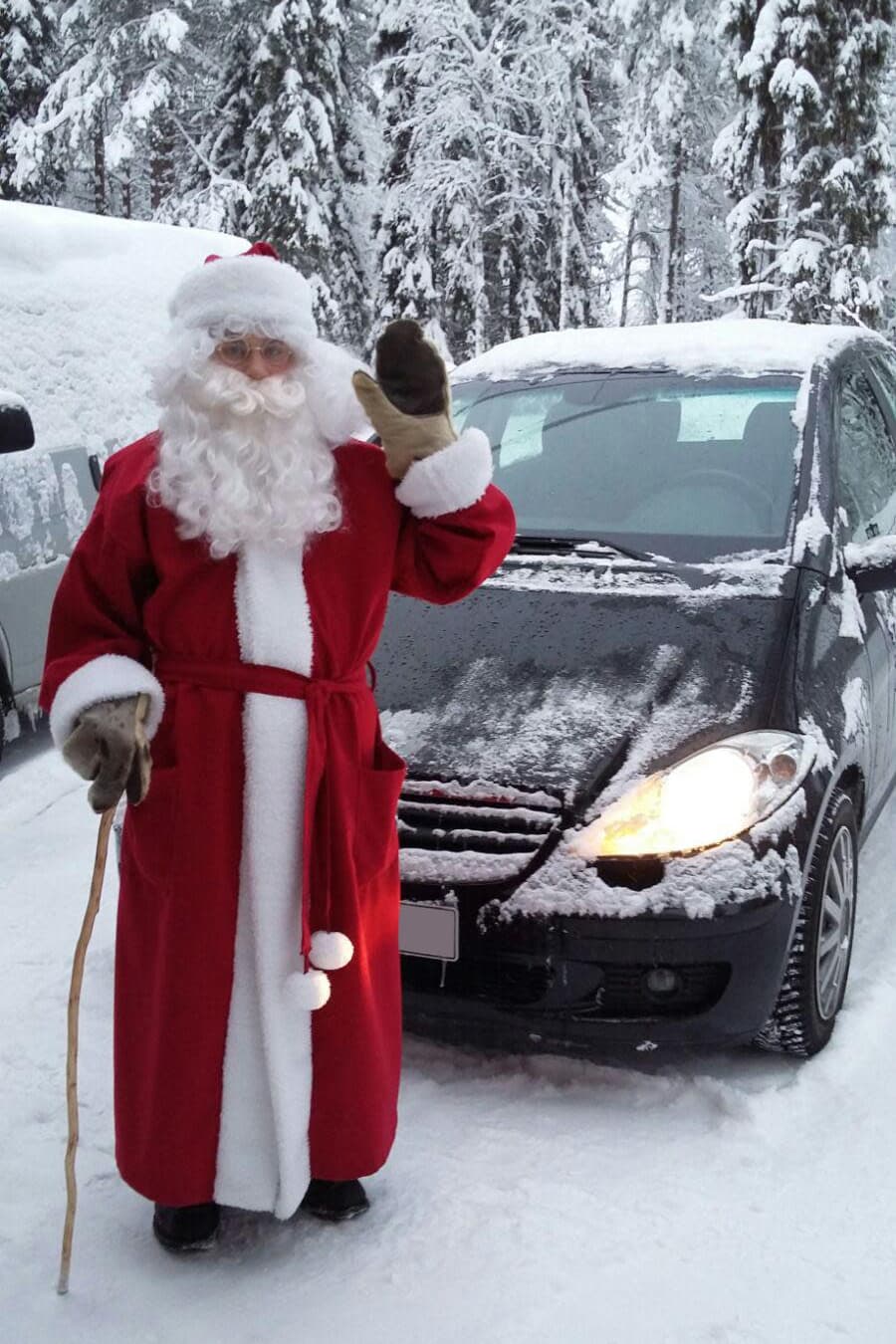 Riku Oikarinen, 21, on pukeutunut joulupukiksi ja vilkuttaa kameralle. Hänen takanaan on auto ja luminen maisema.