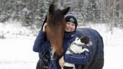 Emma hevoshaassa kainalossaan koira Zoja sekä hevonen Aurora Comery.
