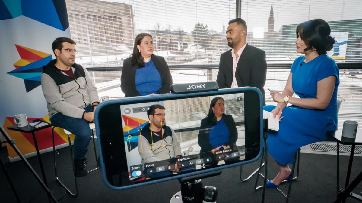 Neljä ihmistä TV-studiossa. Ikkunasta näkyy Eduskuntatalo.