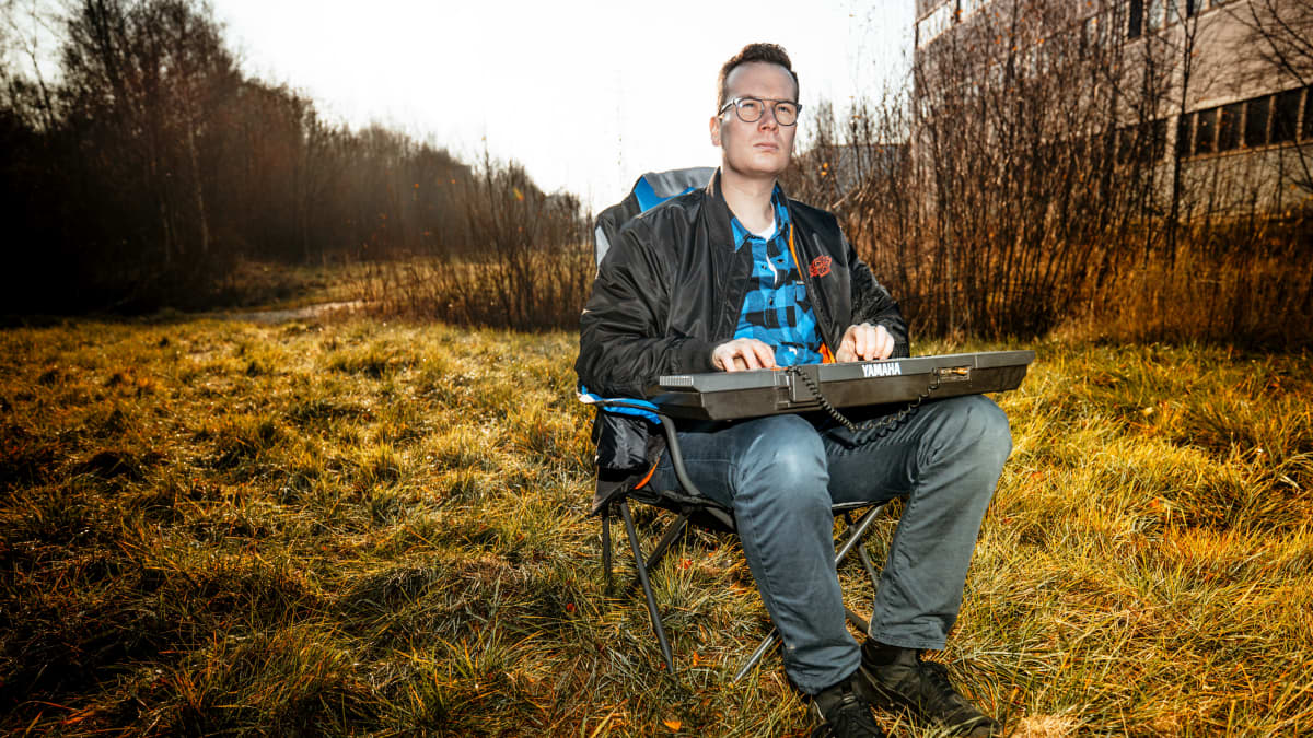 Janne Rintala istuu kosketinsoitin polvilla nurmikolla tyhjällä tontilla.
