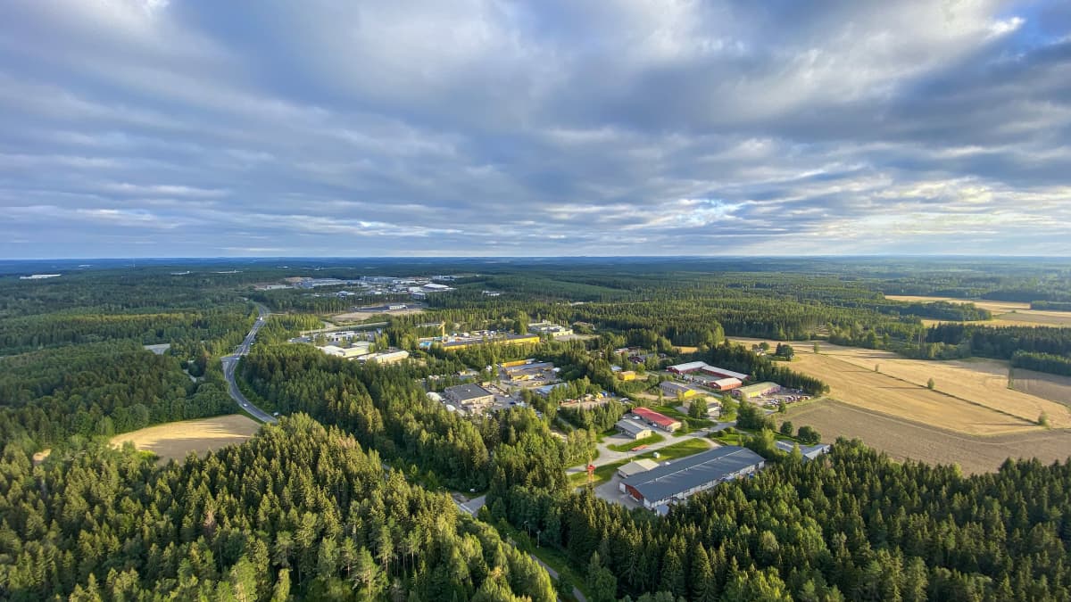 Pelto- ja metsämaisemaa kuumailmapallon korista kuvattuna Hämeenlinnassa. Rakennuksiin heijastuu valonsäde sinisen taivaan välistä.