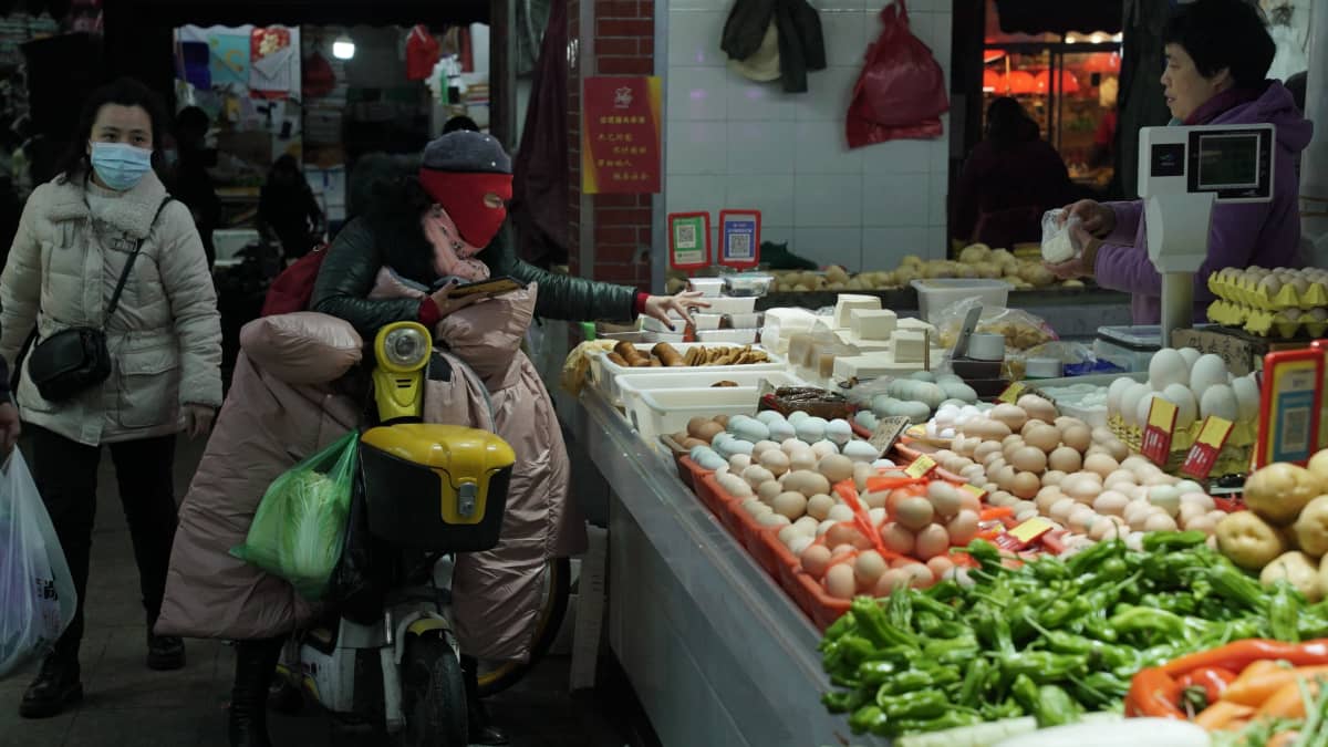 sisätorilla nainen istuu mopon päällä ja ostaa vihanneksia