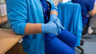 A nurse sitting with her hands in her lap, wearing rubber gloves.
