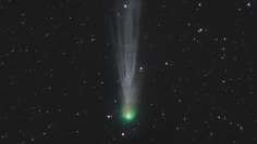 Tähtitaivaalla komeetta, vihreänä johtava valopallo, jonka perässä himmeämpi valo pyrstö.