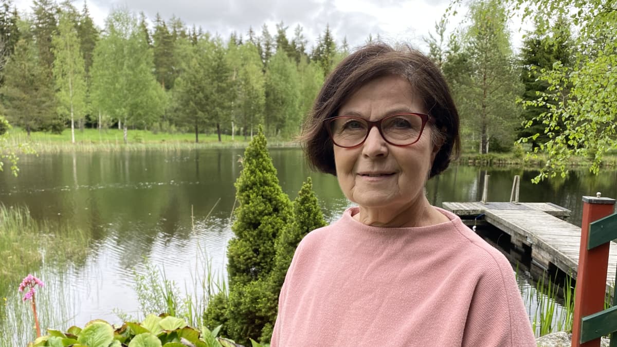 Suomen kielen emeritaprofessori Kaisa Häkkinen seisoo lammen rannalla.