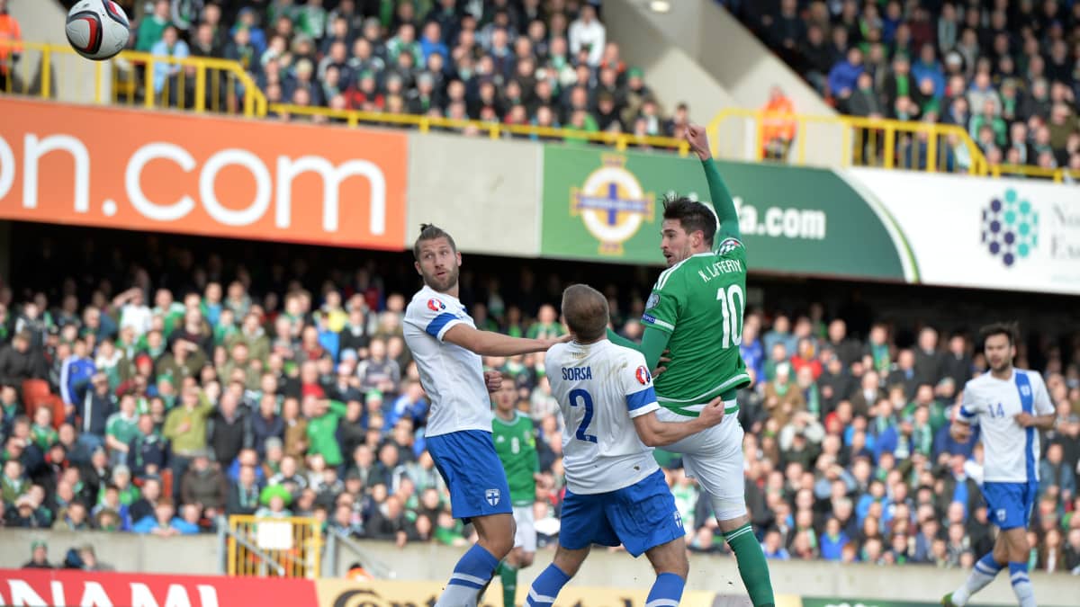 Pohjois-Irlannin Kyle Lafferty puskee pallon maaliin EM-karsintaottelussa Suomea vastaan 29. maaliskuuta 2015. Sebastian Sorsa ja Joona Toivio jäävät kakkoseksi.