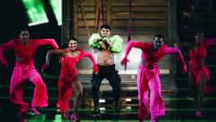 Käärijä iklädd grön bolero står och dansar med sina fyra dansare klädda i ljusröda kläder.