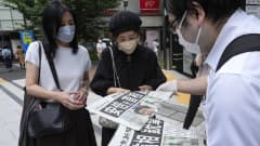 Kolme japanilaista ihmistä lukee kadulla sanomalehdestä entisen pääministerin kuolemasta.