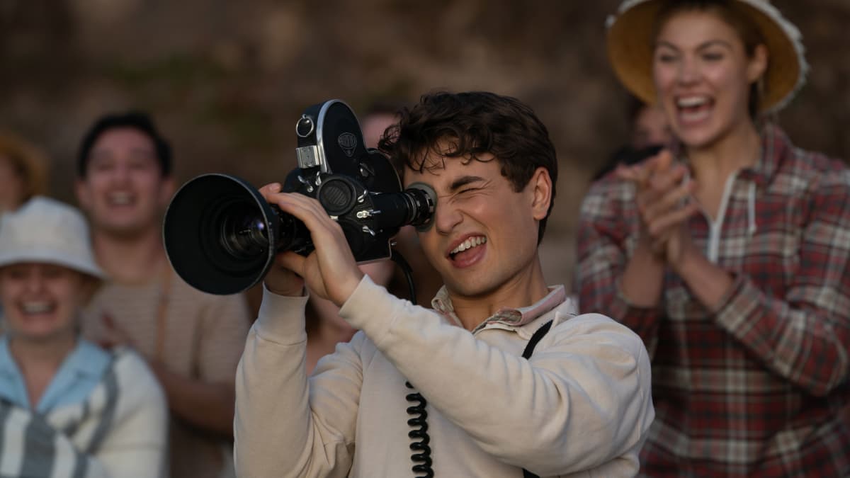 En ung man håller i en filmkamera medan människor omrking honom jublar.