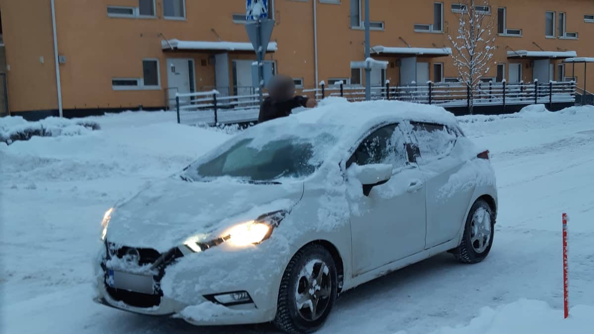Mies puhdistaa auton kattoa lumesta.