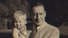 Nuori Hannu Hallamaa isänsä sylissä vanhassa valokuvassa.