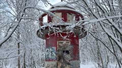 Oulussa sijaitseva vanha punainen ja osin töhritty merimerkki, Taskilan loisto, lumisten puiden keskellä.
