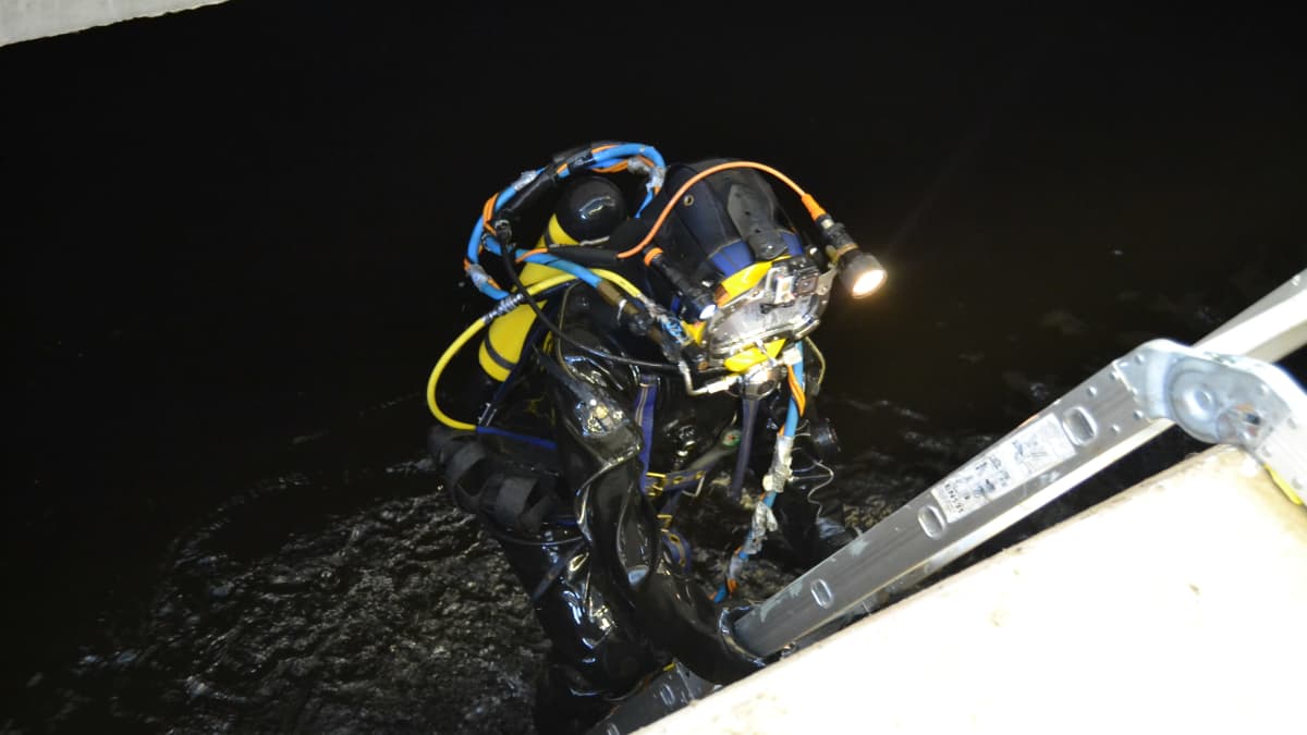 Pelastussukeltaja Kari Back menossa tikapuita pitkin tummaan veteen.