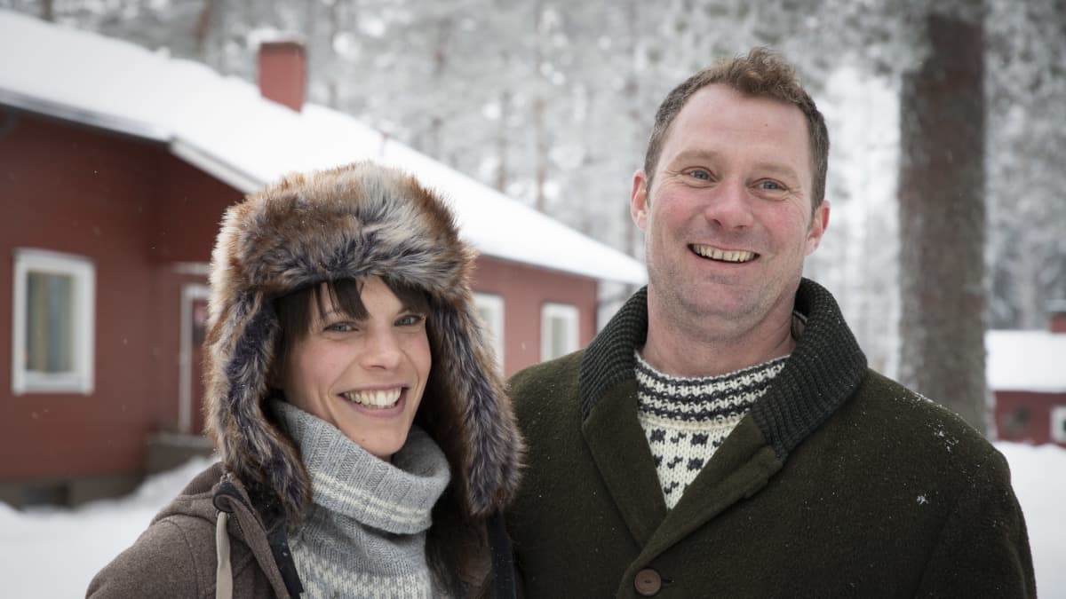 Elin ja Erkki Kinnunen poseeraavat kameralle ja hymyilevät kotitalonsa edessä talvimaisemassa.