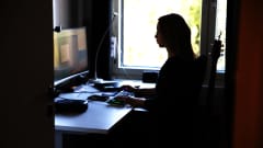 Nainen tekee kotonaan töitä tietokoneella. Naisesta näkyy siluetti ikkunaa vasten.