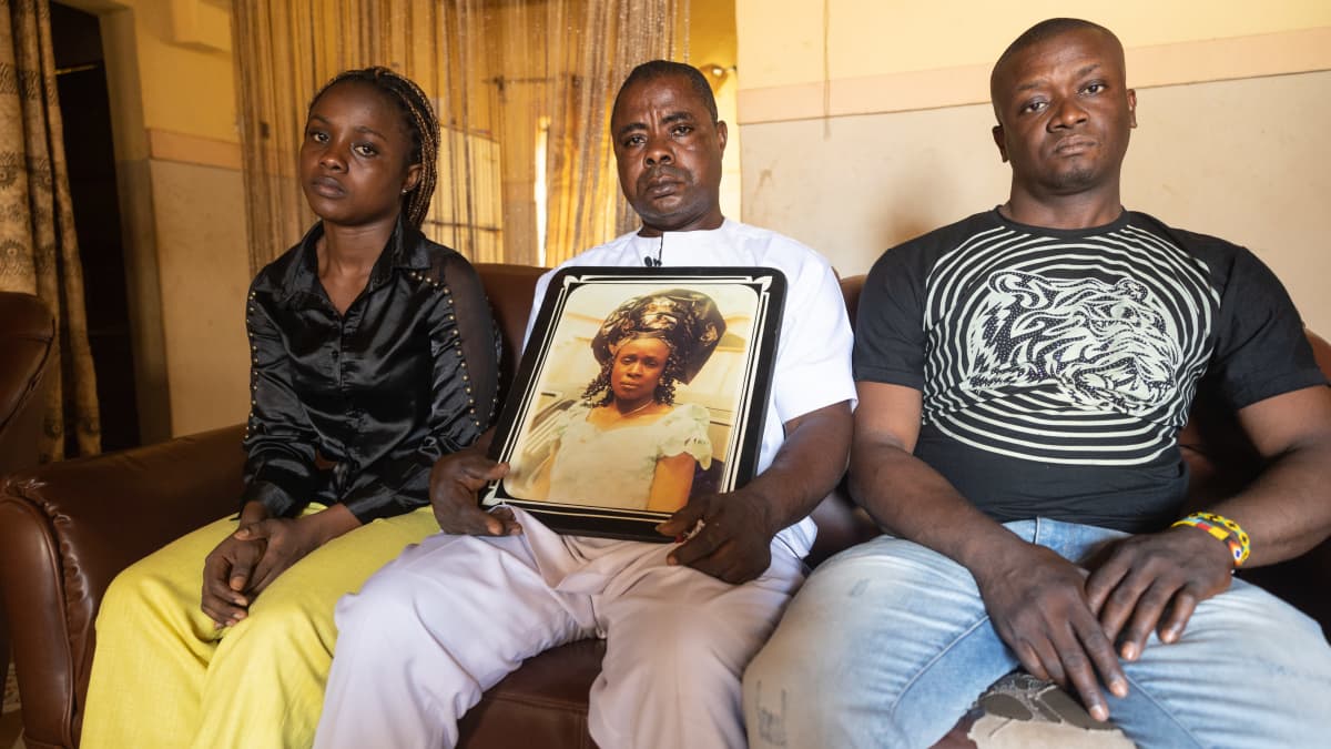 Nigerialaiset aikuiset tytär, isä ja poika istuvat sohvalla, isän sylissä perheen kuolleen äidin valokuva, 
